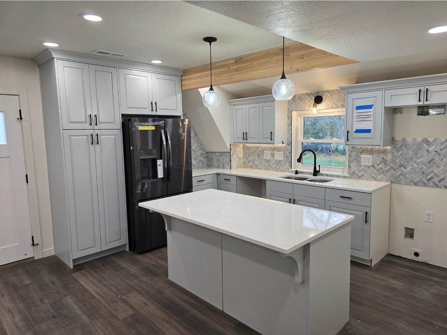 Modern open-concept kitchen remodel with light gray shaker cabinets, quartz island, and herringbone backsplash